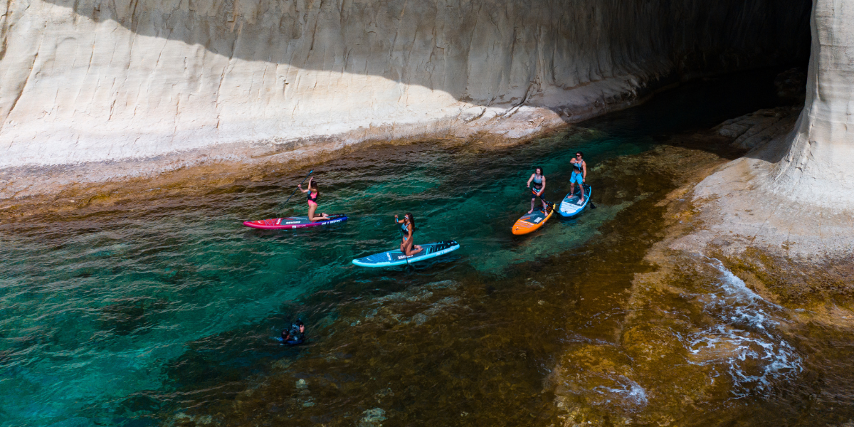 Four people paddleboarding next to some cliffs