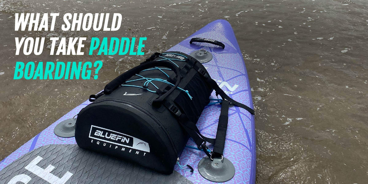 Paddleboard violet avec sac d’équipement noir en eau peu profonde, et texte demandant quoi emporter pour pagayer