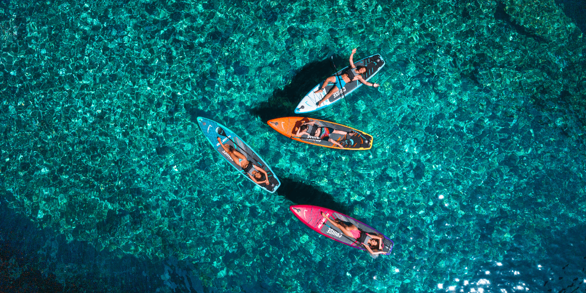 Quatre personnes pagaient sur des stand-up paddles colorés dans une eau turquoise limpide, vues du dessus