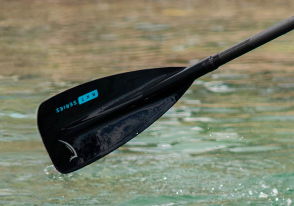 Black paddle blade partially submerged in water, featuring blue text 'NXT SERIES' on the surface.