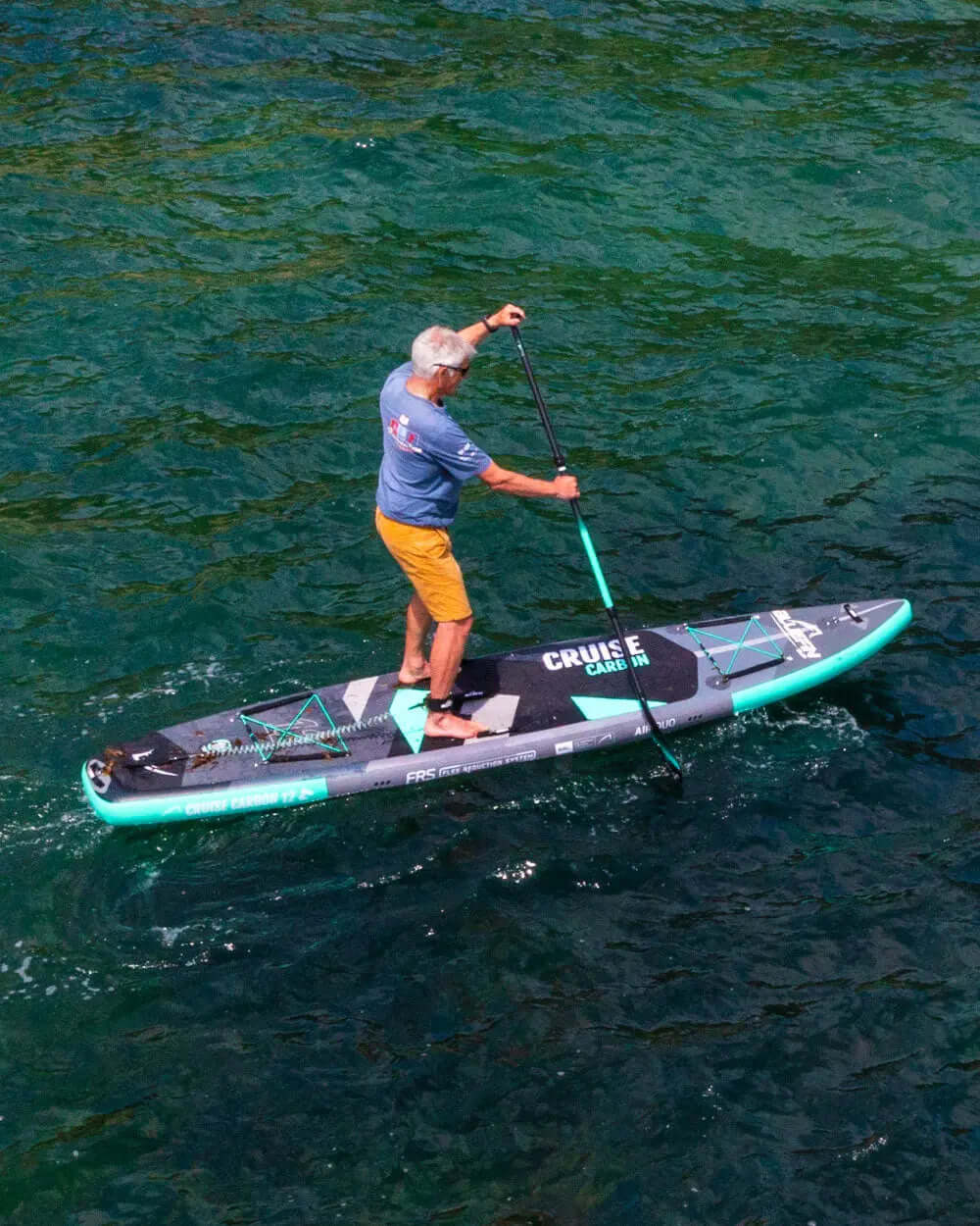 Person paddling on a black and teal inflatable paddleboard in clear water