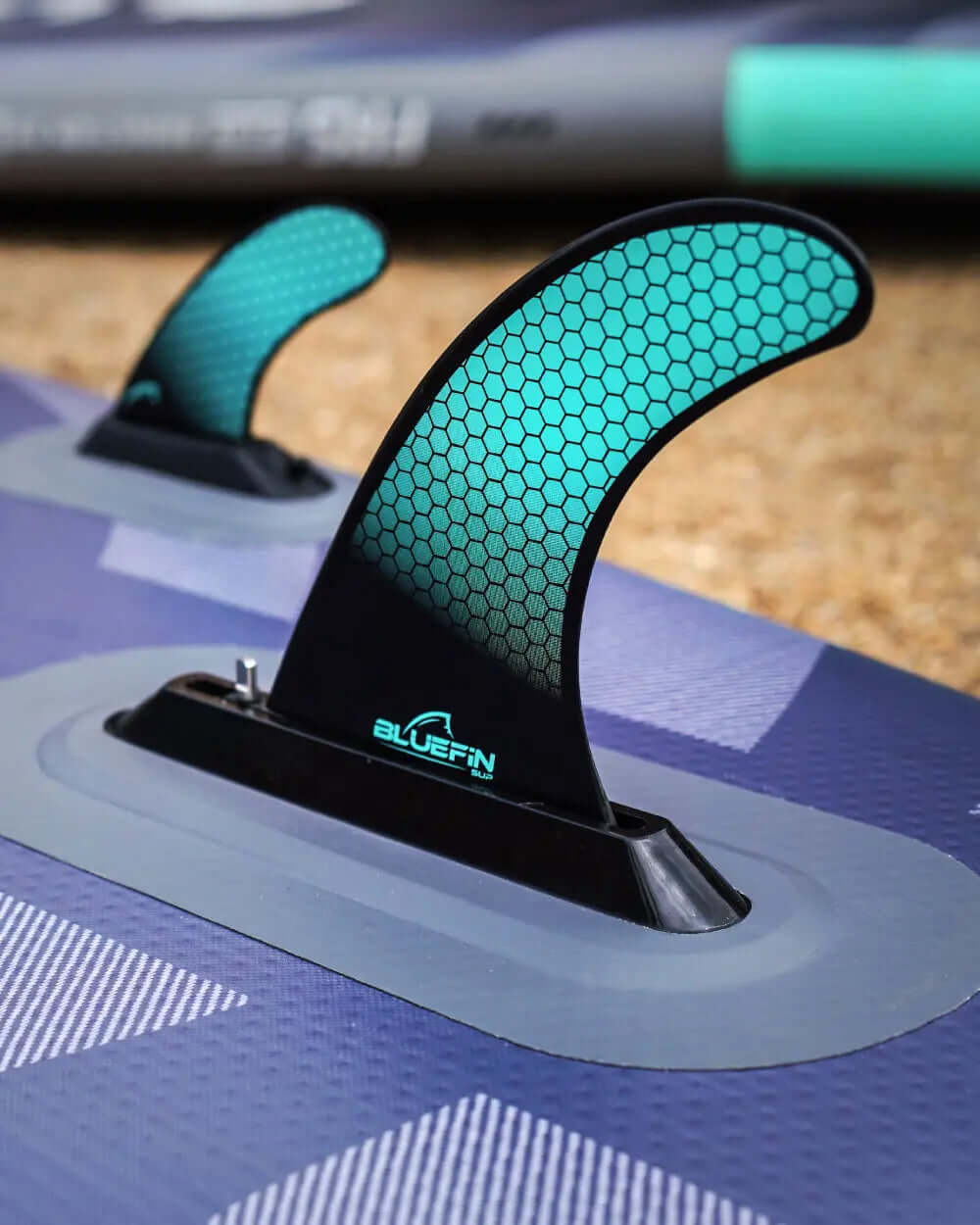 Close-up of a paddleboard fin with a honeycomb design, mounted on a textured surface.