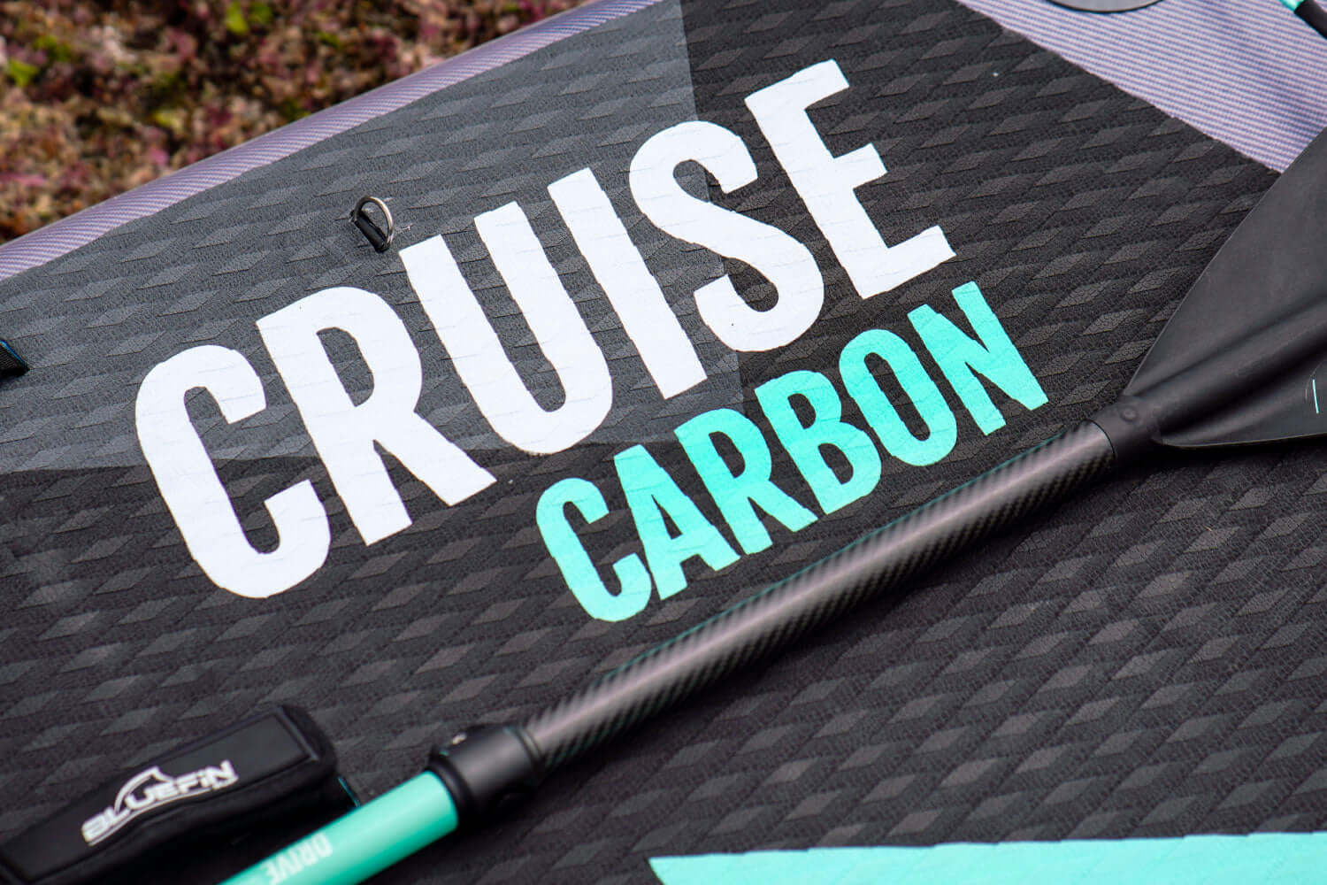 Paddleboard deck featuring the words 'CRUISE CARBON' and a black paddle with a teal shaft