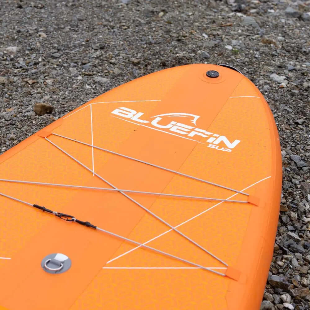 Paddleboard gonflable en orange vif avec surface texturée et rangement par cordon élastique sur le dessus.