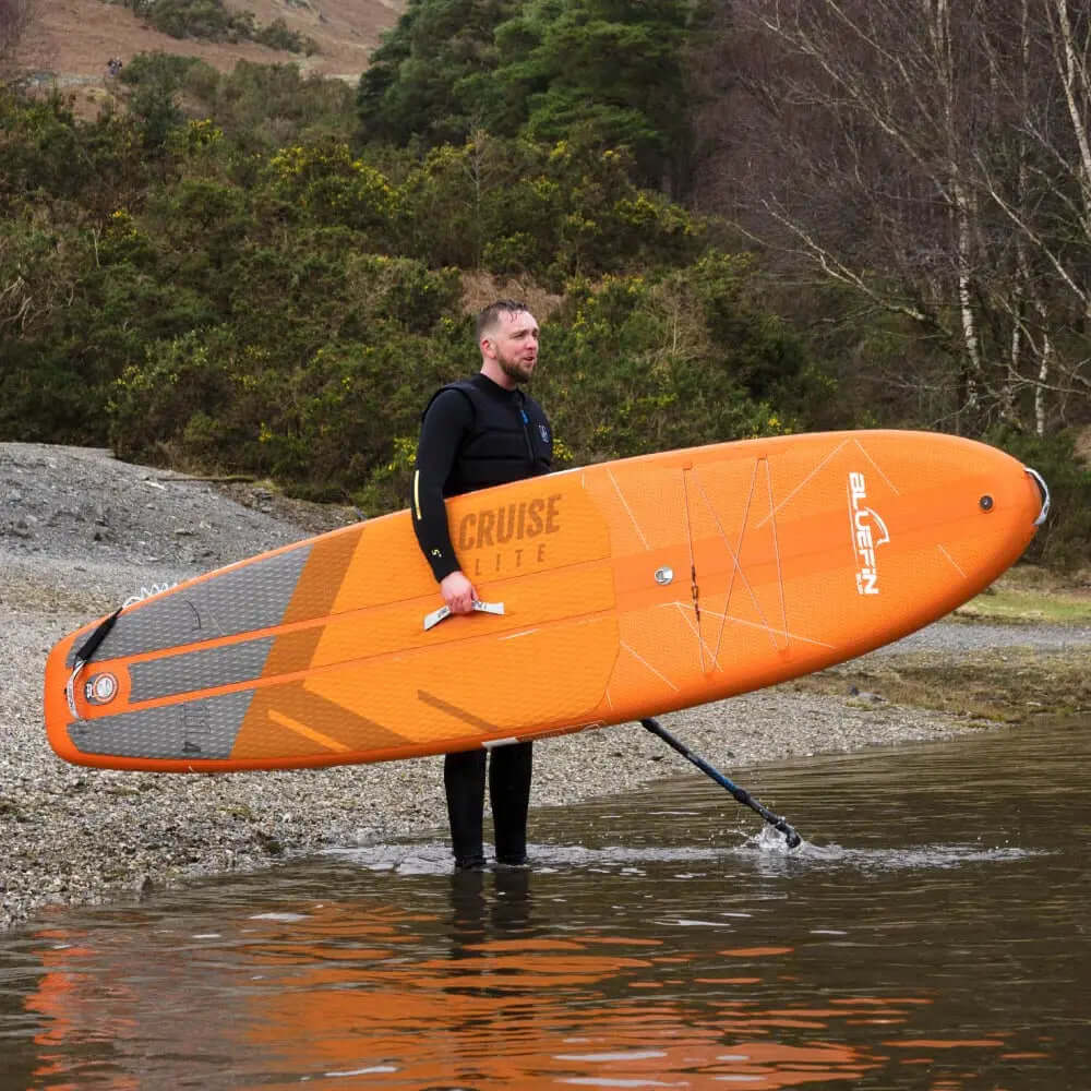Personne debout dans l'eau tenant un paddleboard gonflable orange avec surface texturée et dérive centrale.