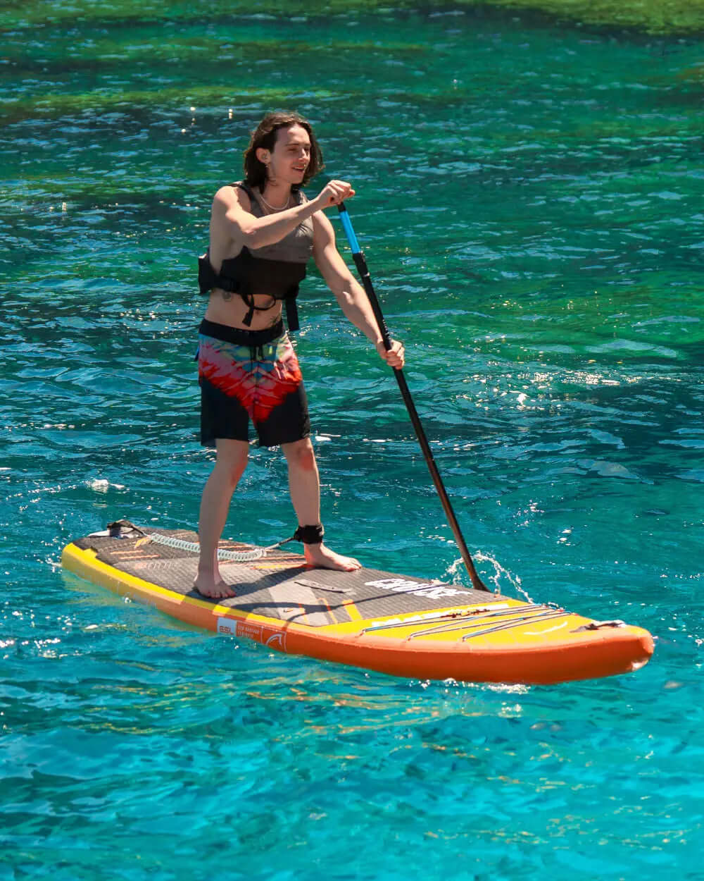 Person paddling on an inflatable stand-up paddleboard in clear turquoise water