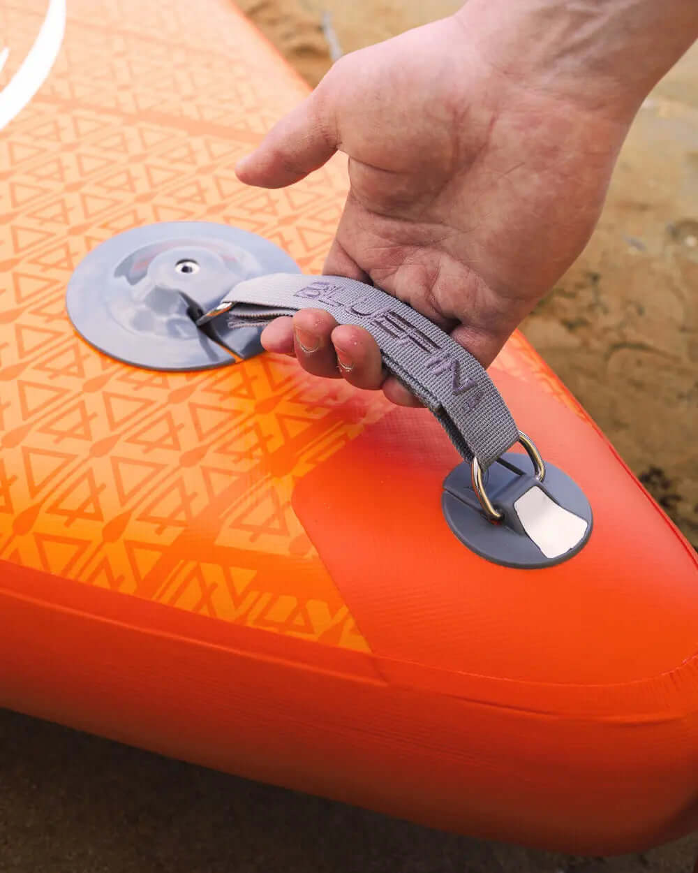 Hand holding the gray strap of an inflatable paddleboard with an orange patterned surface