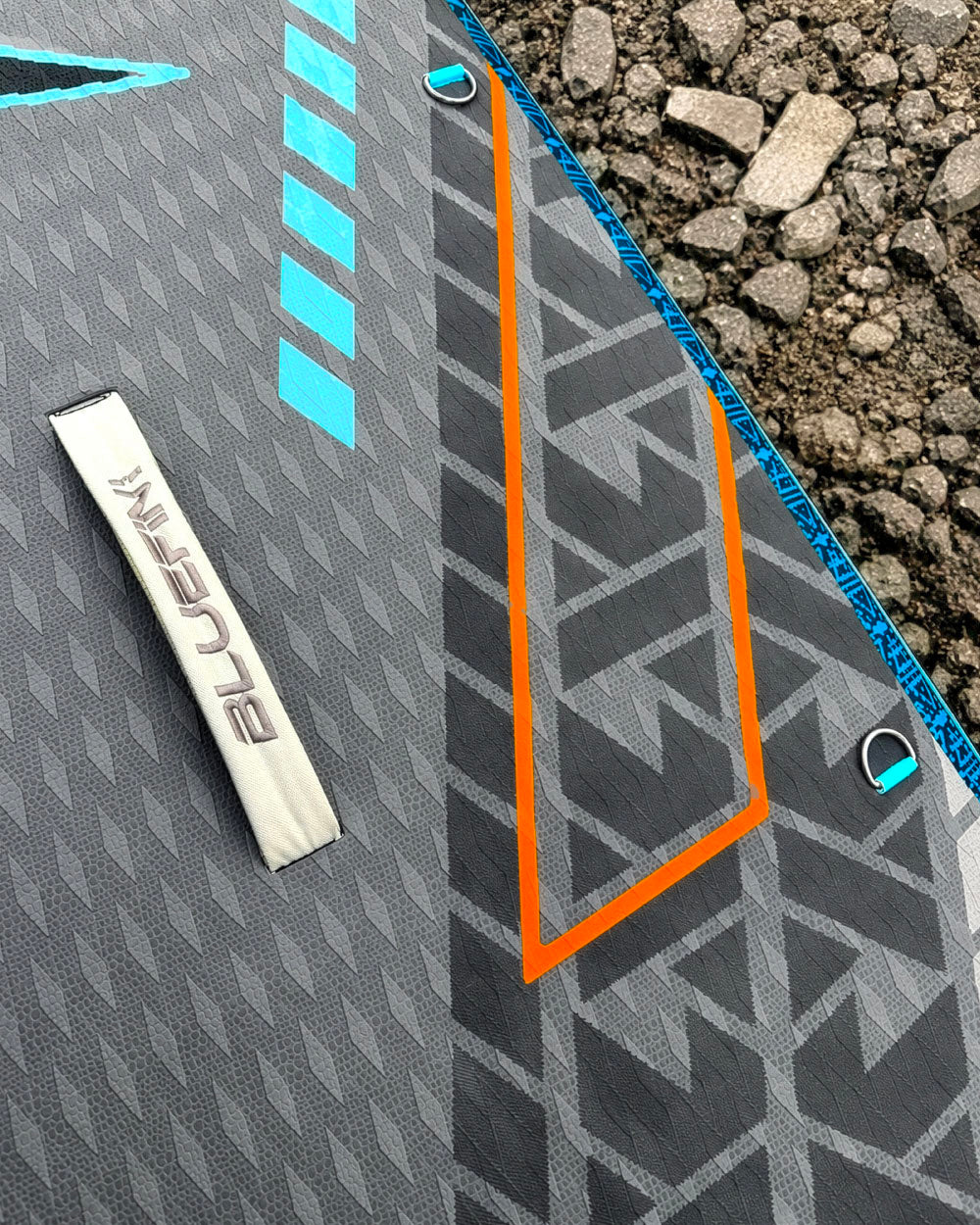Inflatable paddleboard featuring a textured surface, blue and orange graphics, and a metal D-ring.