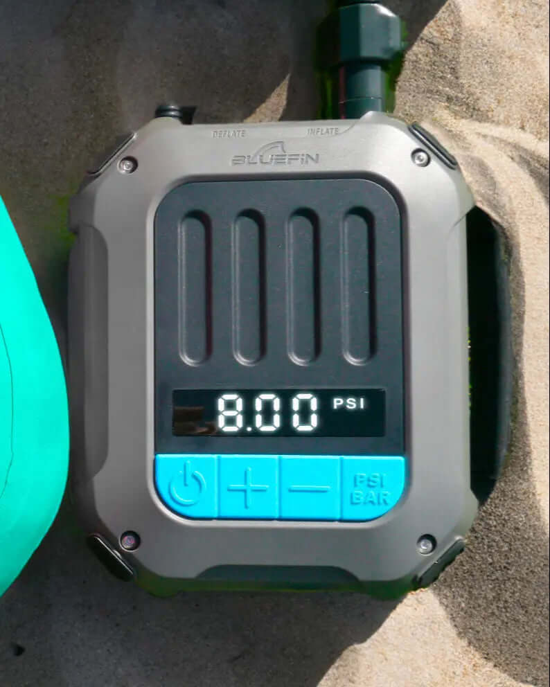 Digital pressure gauge displaying 8.00 PSI, with inflate and deflate buttons, on sandy surface.