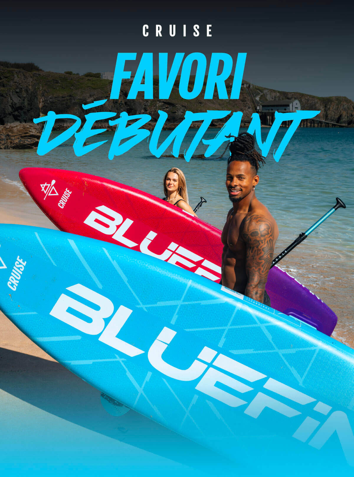 Two paddleboarders on a beach, one with a blue board and the other with a red board, smiling.