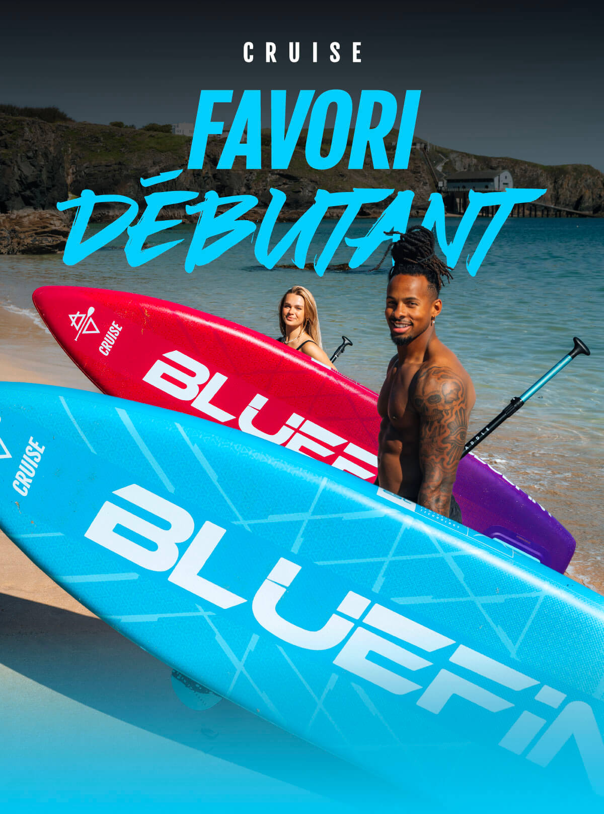 Two paddleboarders on a beach, one with a blue board and the other with a red board, smiling.