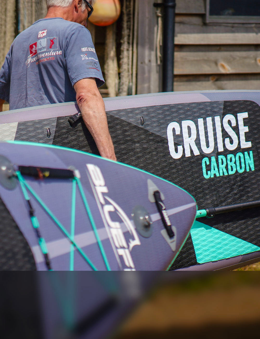 Person carrying a Bluefin Cruise Carbon paddleboard with a textured deck and center fin