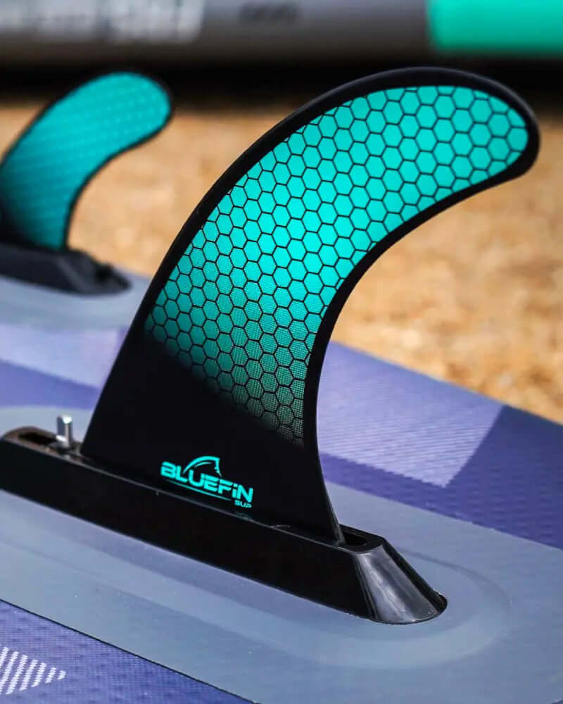Close-up of a paddleboard fin with a honeycomb pattern and BLUEFIN logo on a textured surface