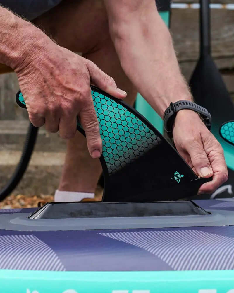 Person attaching a black fin to an inflatable paddleboard with a textured surface