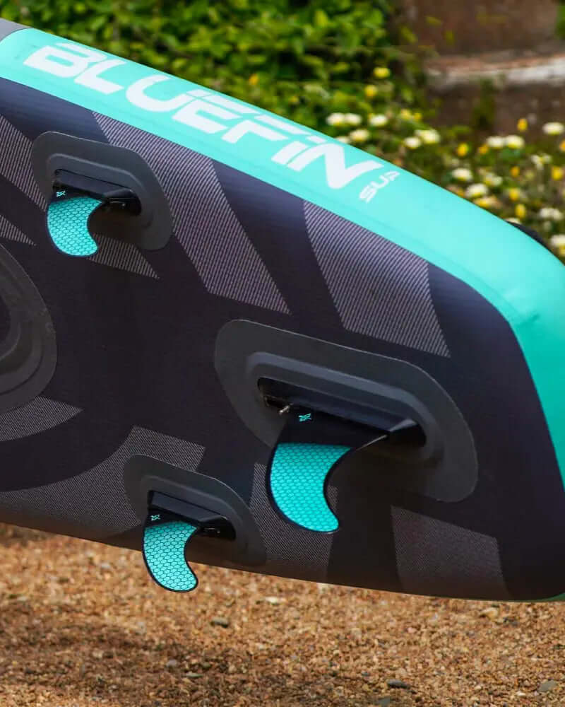 Inflatable paddleboard showing two fins, textured surface, and branding in teal and black colors