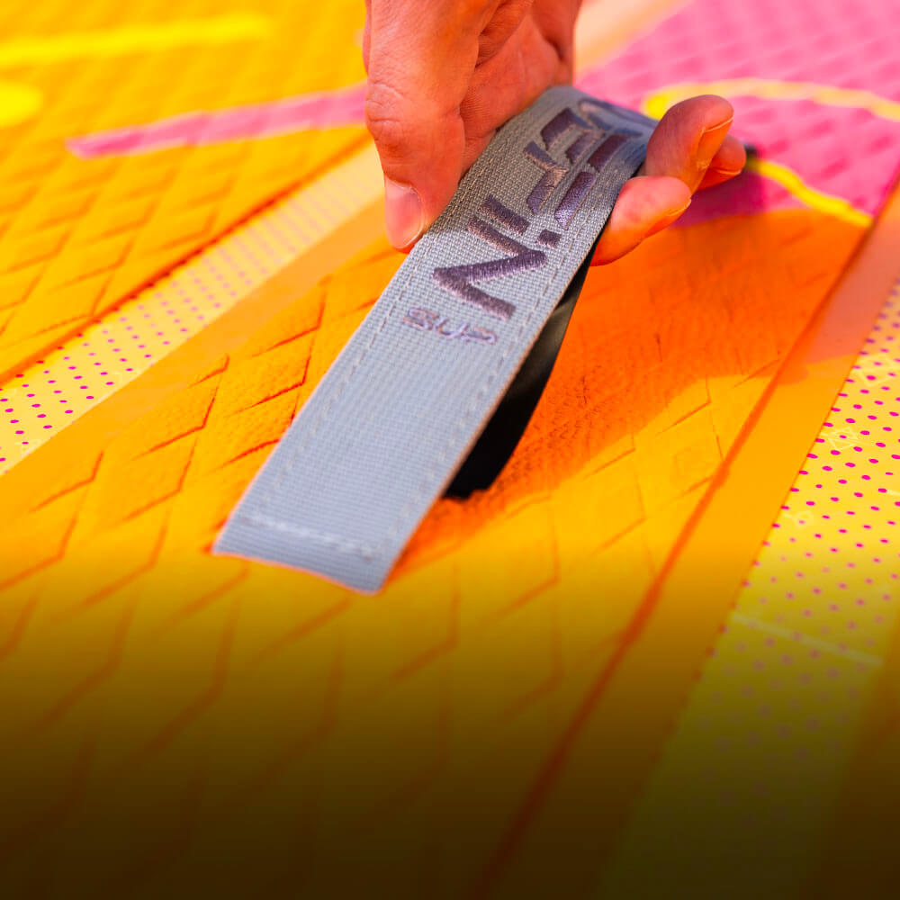 Hand holding a gray strap on a colorful inflatable paddleboard deck with textured surface.
