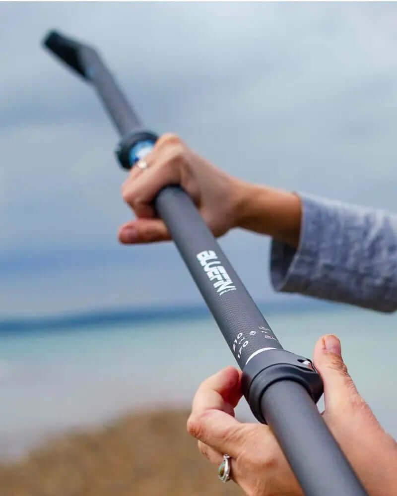 Person holding a black adjustable paddle with a textured grip and a bent end, against a cloudy sky.