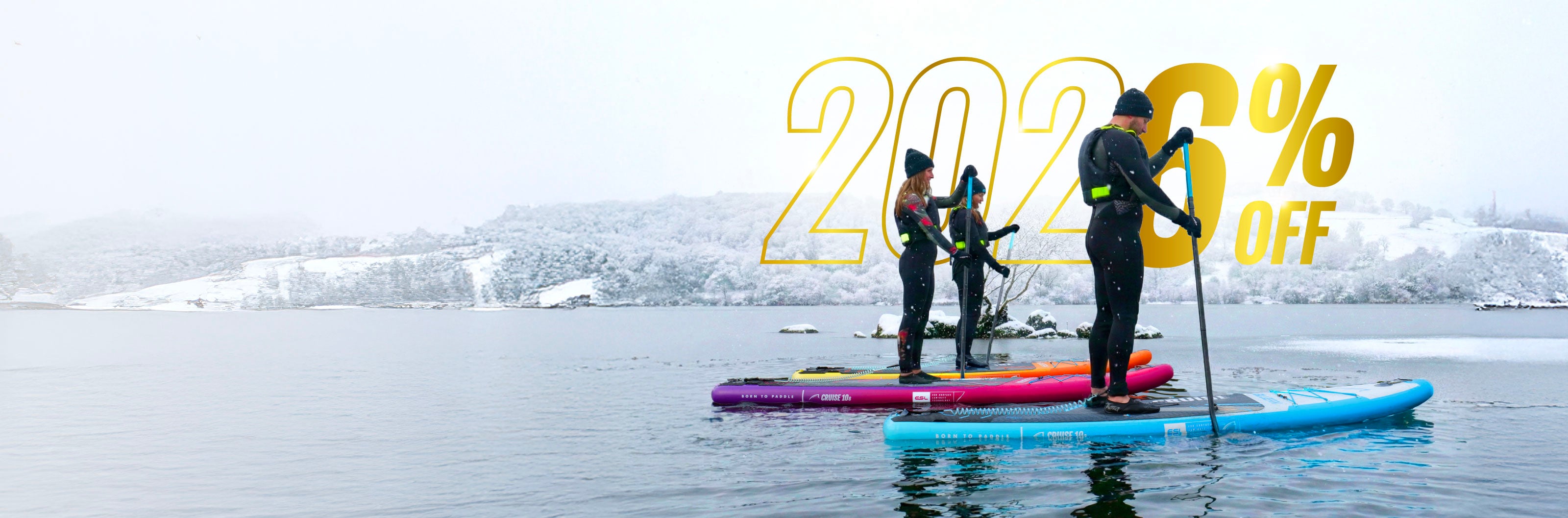 Three paddleboarders on colorful boards in a snowy landscape, paddling on calm water.