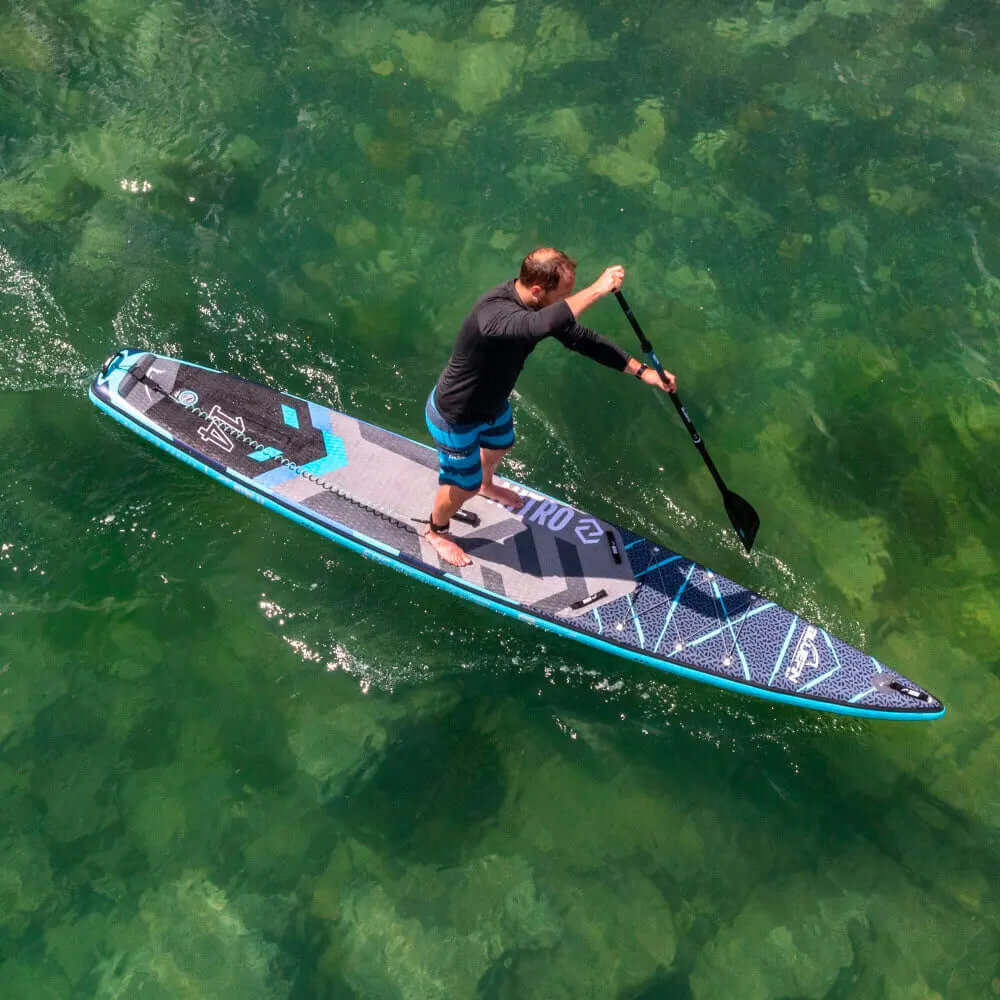 Homme pagayant sur une planche à pagaie gonflable bleu et noir au-dessus d'une eau verte claire
