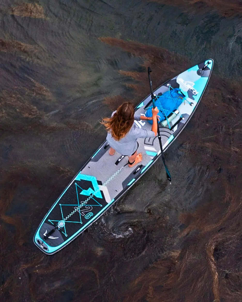 Person paddling an inflatable paddleboard with a blue and gray design on calm water