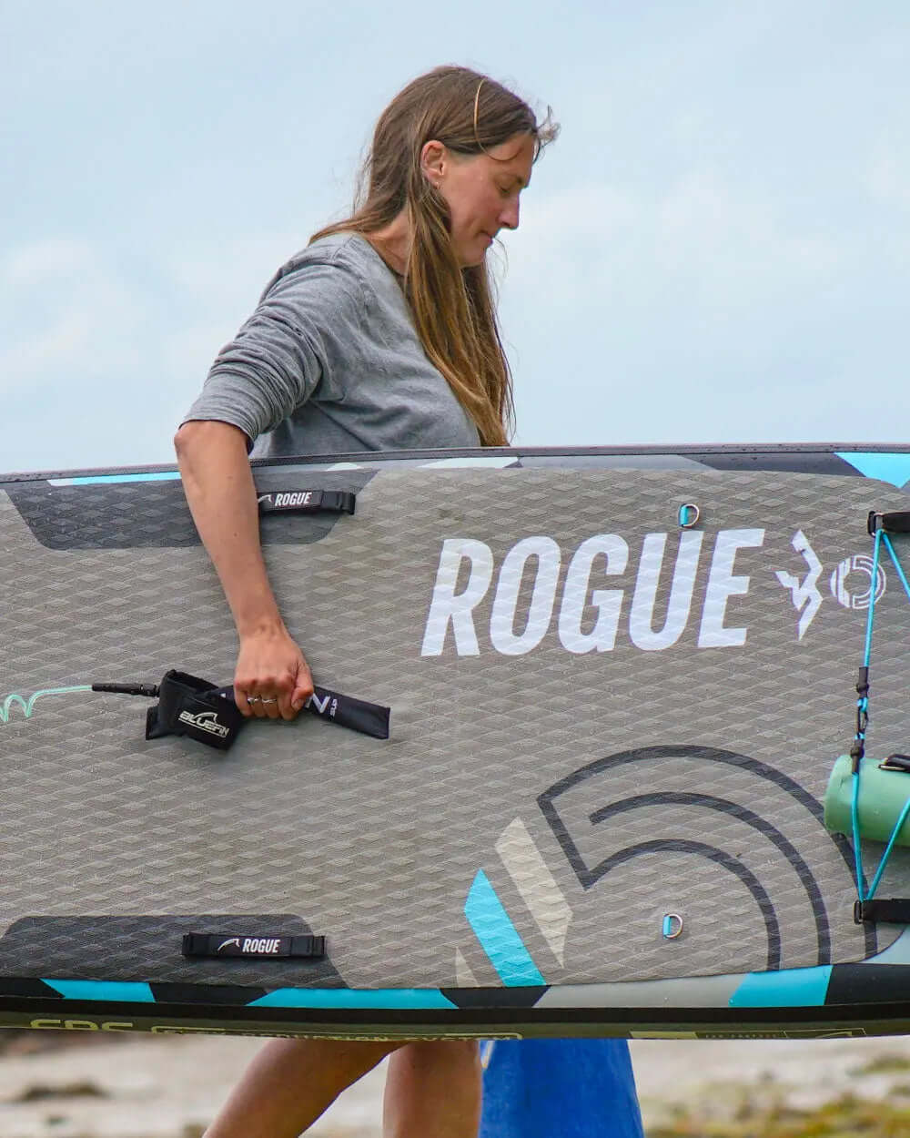 Person carrying a Rogue inflatable paddleboard with textured surface and center fin