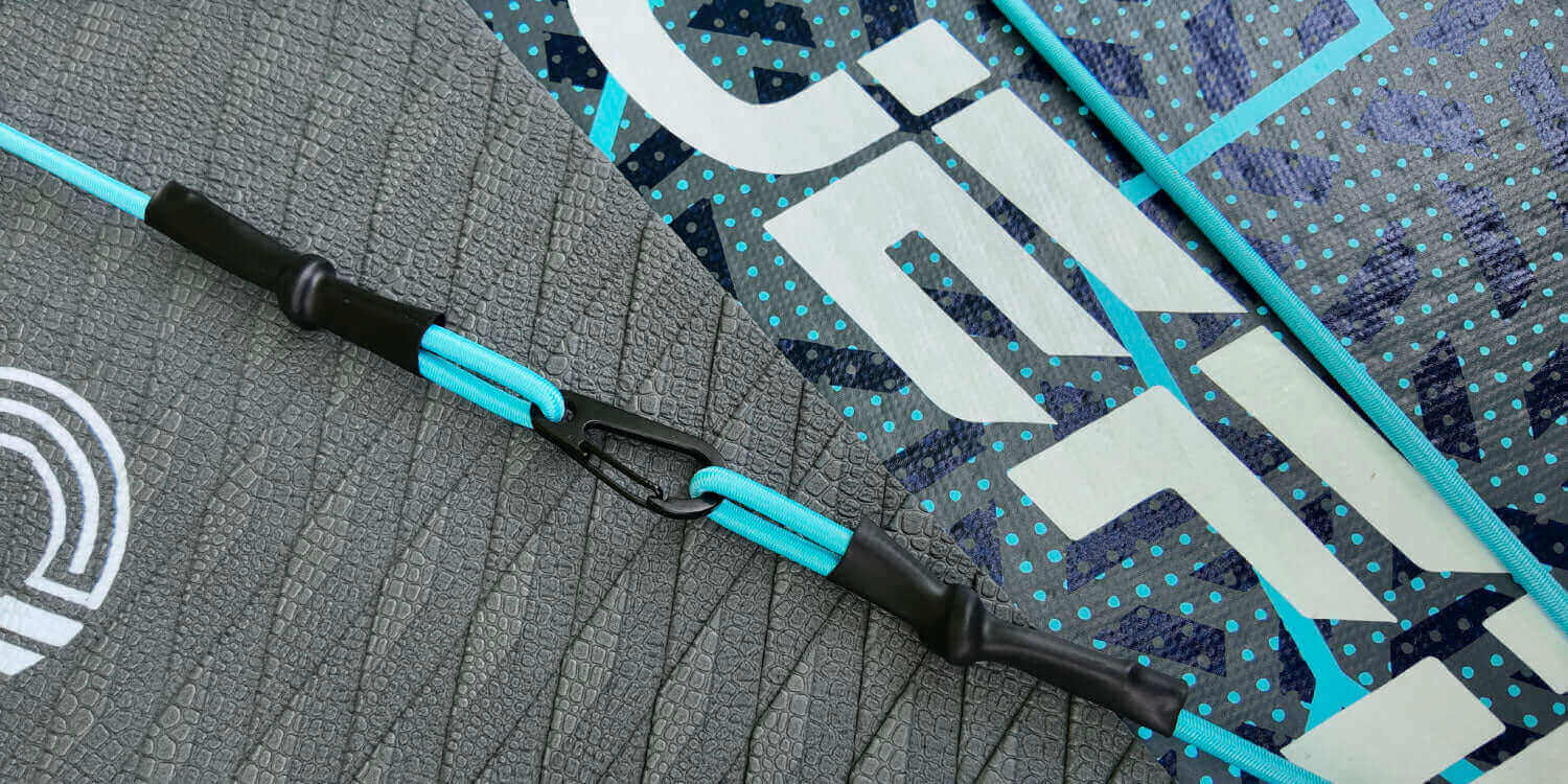 Close-up of a paddleboard's textured surface, featuring a blue safety leash and attachment clip.