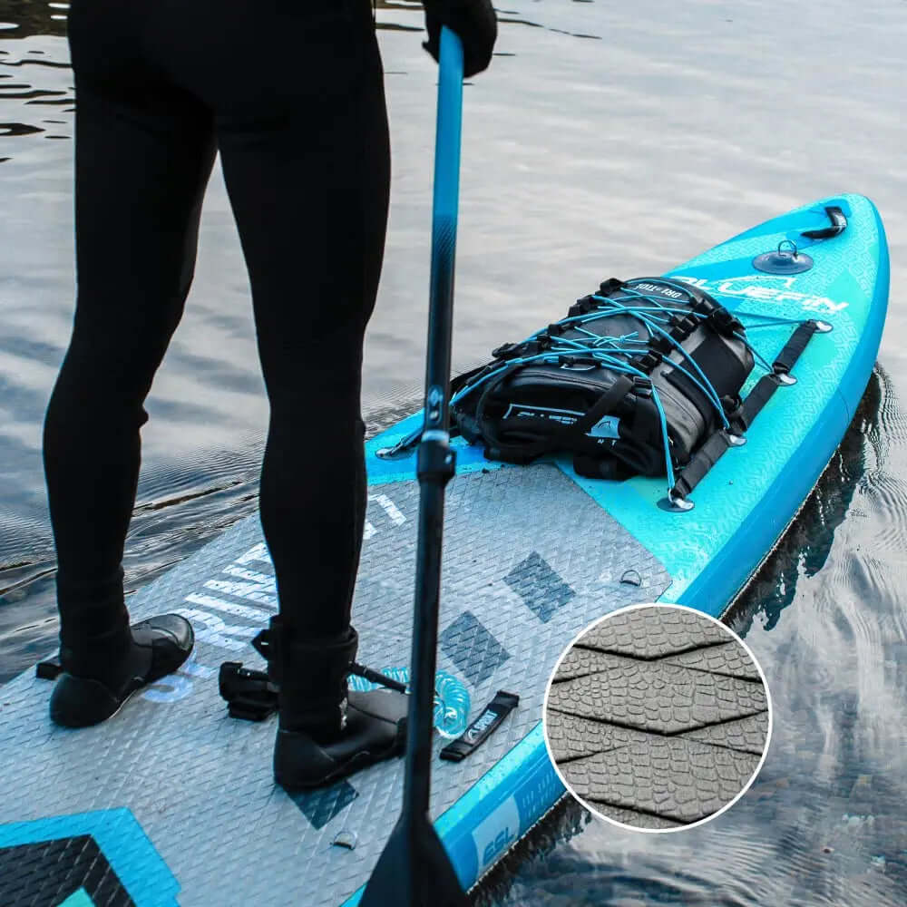 Paddleboard avec un pad de pont texturé, sac à dos noir sécurisé, personne tenant une pagaie dans l'eau