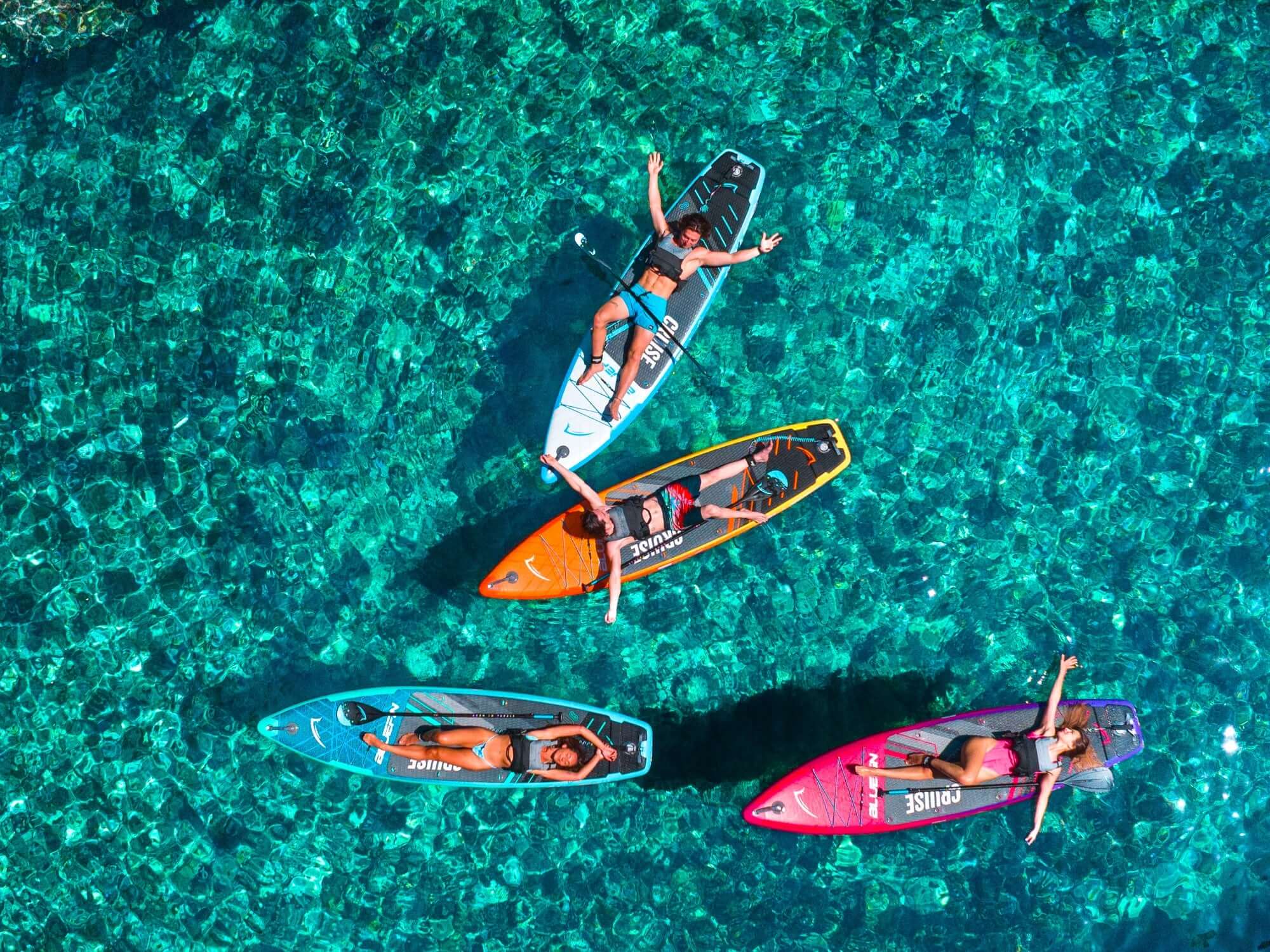 Four paddleboarders relaxing on colorful boards above clear turquoise water