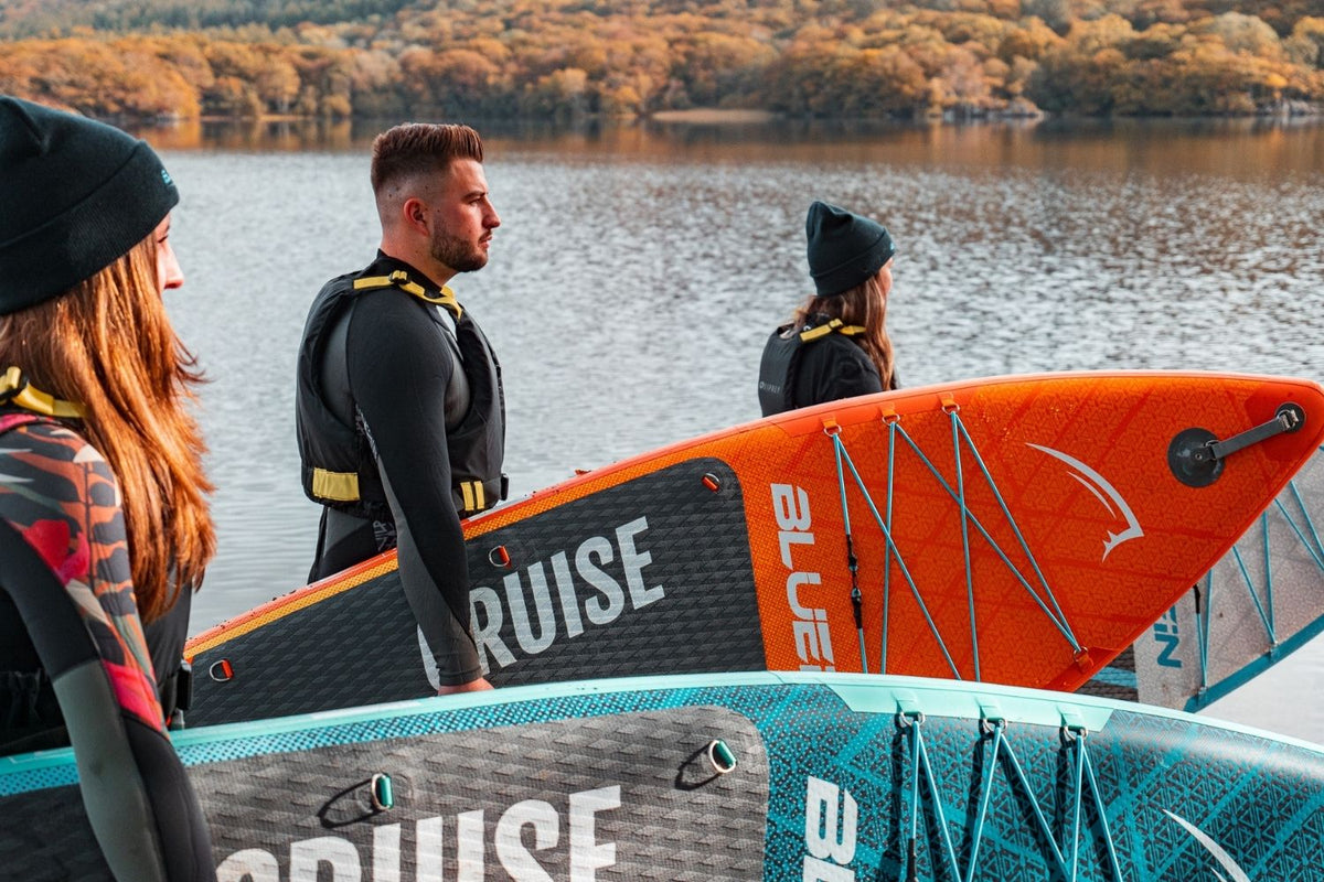 three people holding their paddleboards with the background being autumnal