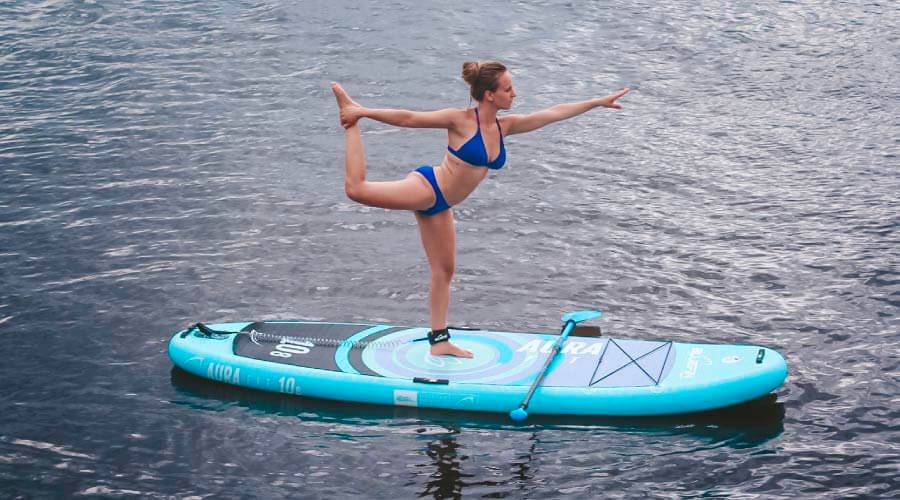 Woman in a blue bikini performing a yoga pose on a turquoise paddleboard in calm water