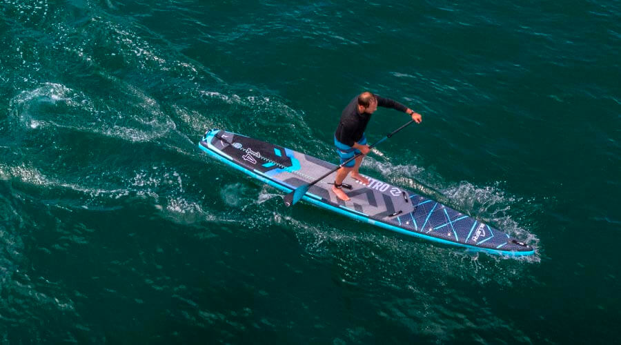 Person paddling on a blue inflatable stand-up paddleboard in clear water