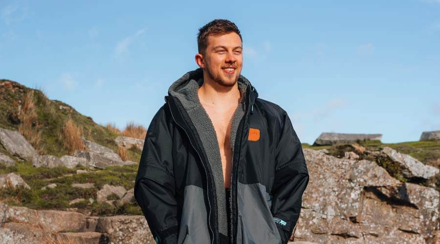 Man wearing a black jacket with gray lining, standing on rocky terrain under a blue sky.