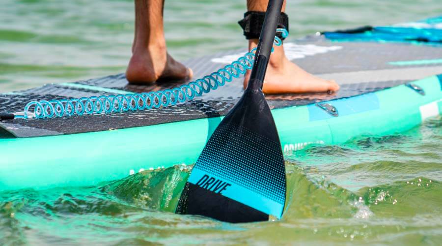 Person standing on a paddleboard with a black paddle in the water, turquoise coil leash attached.