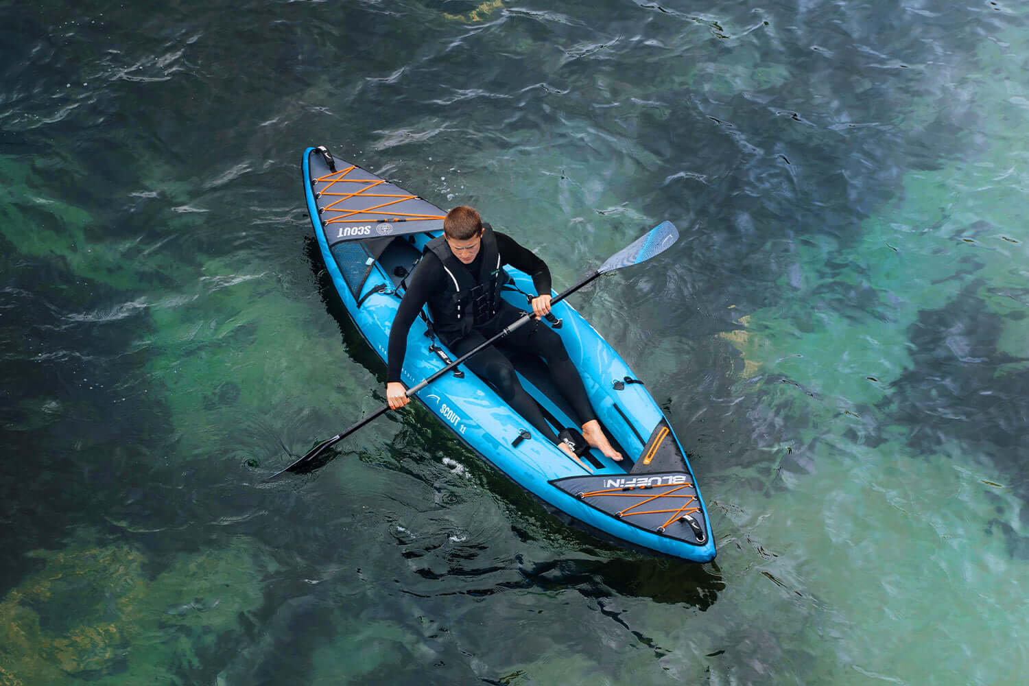 Person paddling a blue inflatable kayak on clear water, wearing a wetsuit and life jacket.
