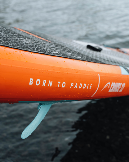 Close-up of orange inflatable paddleboard with textured deck, fin, and water droplets