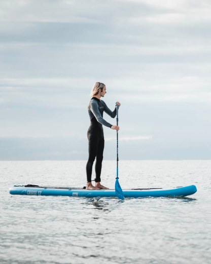 Person in wetsuit paddling on a blue inflatable paddleboard in calm water