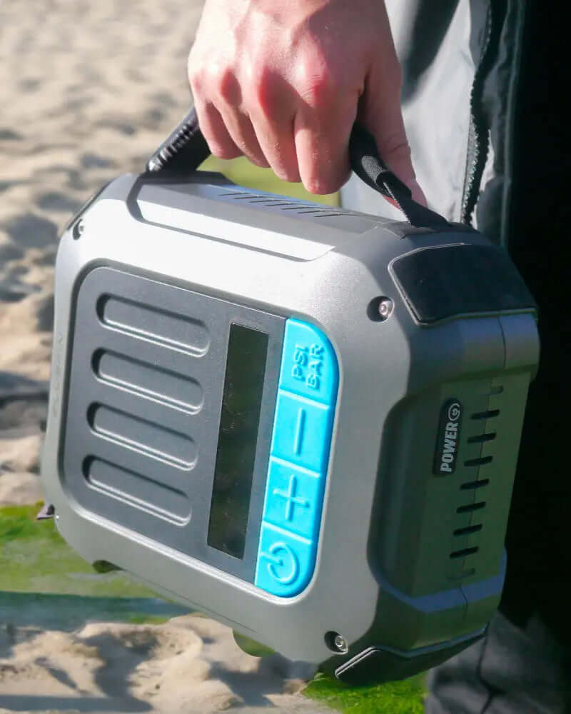 Portable air pump with blue control panel, being held on a sandy beach.