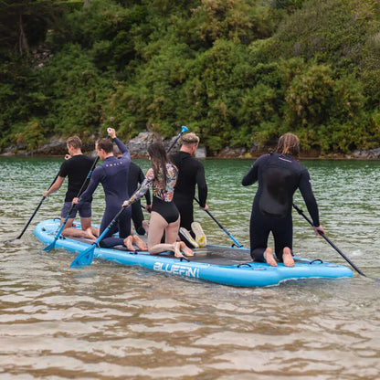 Groupe de six personnes pagayant sur un paddleboard gonflable bleu dans une eau calme